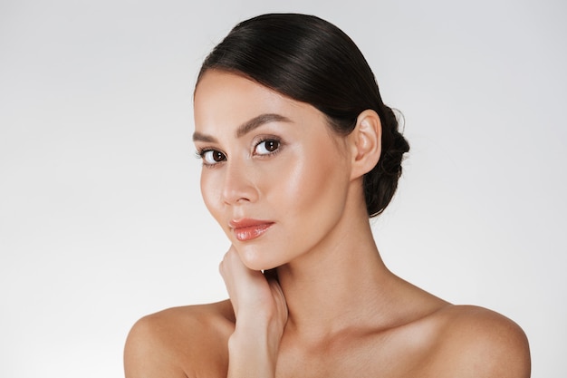 Retrato de belleza de encantadora mujer caucásica con cabello castaño en moño posando a la cámara con hermosa mirada, aislado en blanco