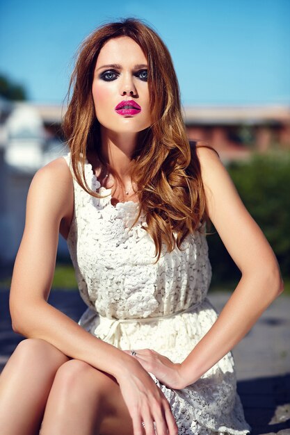 Retrato de belleza glamour de hermosa sensual modelo caucásica joven con maquillaje de noche en vestido blanco de verano posando en la calle