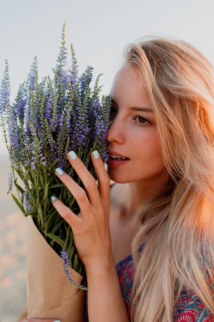 Retrato de belleza de hermosa mujer rubia con ramo de lavanda mirando a cámara. Piel perfecta. Maquillaje natural.