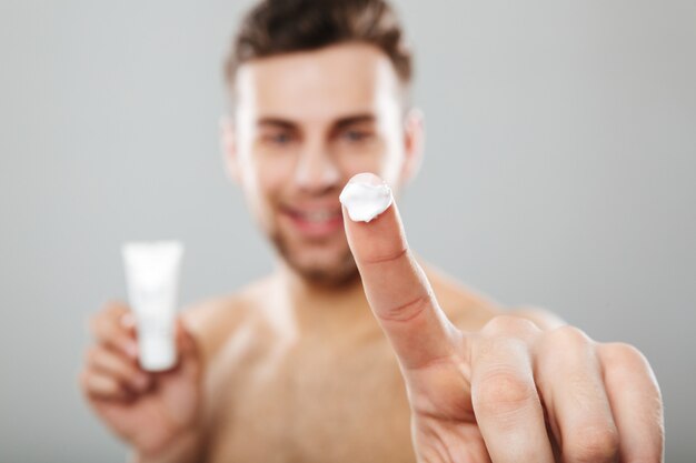 Retrato de belleza de un hombre medio desnudo aplicando crema para la cara