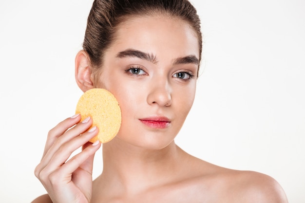 Retrato de belleza de joven semidesnuda con esponja de maquillaje en la cara y mirando