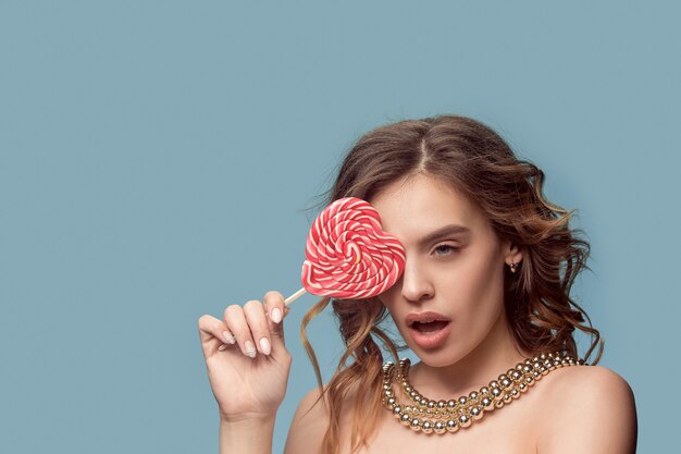 Retrato de belleza de una linda chica en acto para comer un caramelo sobre estudio azul