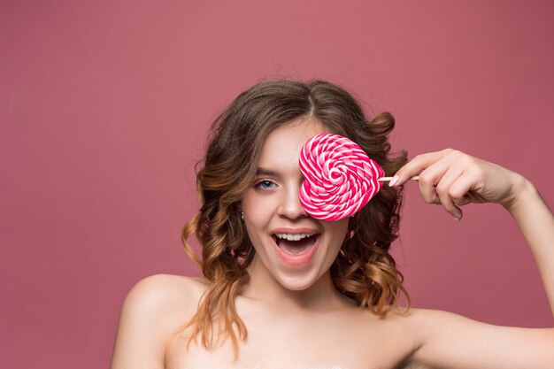 Retrato de belleza de una linda chica en acto para comer un caramelo sobre pared rosa