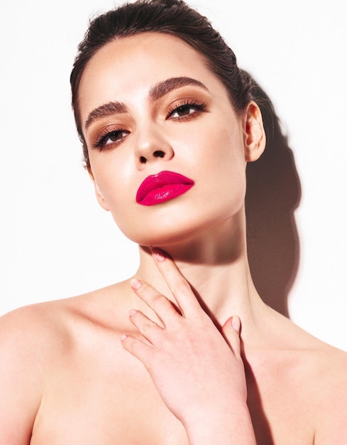 Retrato de belleza de moda de mujer morena joven con maquillaje elegante de noche y piel limpia perfecta Modelo sexy con cabello en un moño posando en estudio Con labios naturales brillantes rosados Aislado en blanco