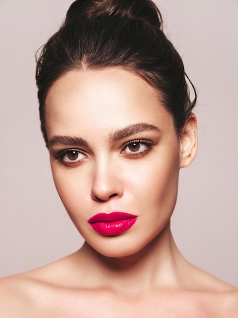 Foto gratuita retrato de belleza de moda de mujer morena joven con maquillaje elegante de noche y piel limpia perfecta modelo sexy con cabello en un moño posando en estudio sobre fondo gris con labios naturales brillantes rosados