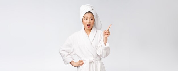 Retrato de belleza de mujer joven mostrando y señalando con el dedo al espacio vacío de la copia belleza asiática en bata de baño