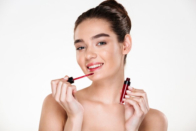 Retrato de belleza de mujer morena caucásica con pelo en bollo aplicando brillo labial mirando