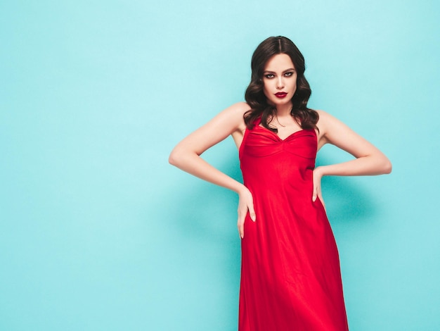 Retrato de belleza de mujer morena joven con maquillaje de noche y piel limpia perfecta Modelo sexy con cabello rizado posando en estudio Con labios naturales rojos brillantes En vestido rojo