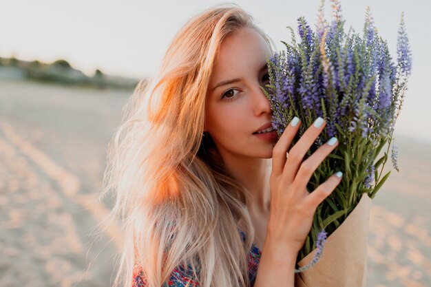 Retrato de belleza de mujer rubia romántica con ramo de lavanda mirando a cámara. Piel perfecta. Maquillaje natural.