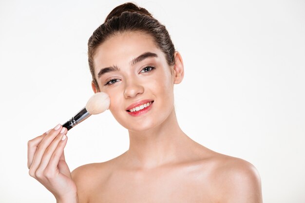 Retrato de belleza de mujer semidesnuda sonriente con piel fresca aplicar maquillaje con cepillo suave y mirando