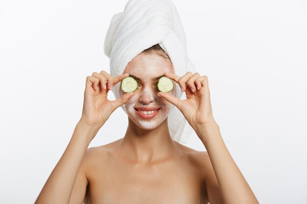 Retrato de belleza de mujer sonriente con toalla en la cabeza y rodaja de pepino en la mano aislado en blanco