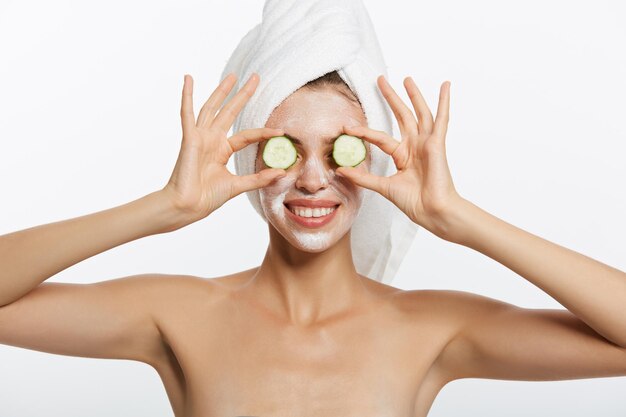 Retrato de belleza de mujer sonriente con toalla en la cabeza y rodaja de pepino en la mano aislado en blanco