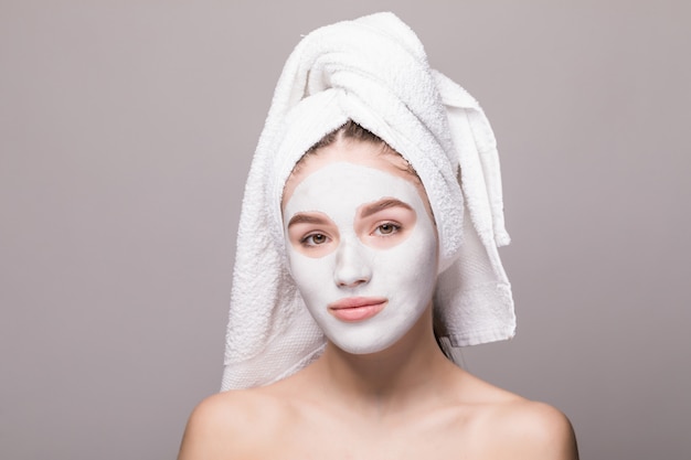 Retrato de la belleza de la mujer en toalla en la cabeza con la máscara o la crema nutritiva blanca en la cara, pared blanca aislada. Cuidado de la piel limpieza eco orgánico cosmético spa relax concepto