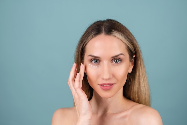 Retrato de belleza de primer plano de una mujer en topless con piel perfecta y maquillaje natural, con puntos de crema antienvejecimiento para hidratar y reafirmar la piel debajo de los ojos