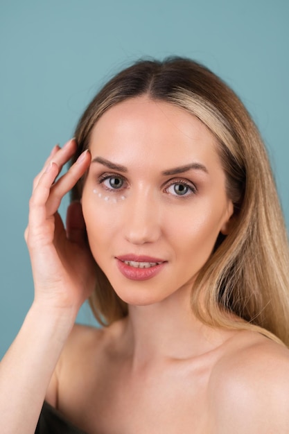 Retrato de belleza de primer plano de una mujer en topless con piel perfecta y maquillaje natural, con puntos de crema antienvejecimiento para hidratar y reafirmar la piel debajo de los ojos