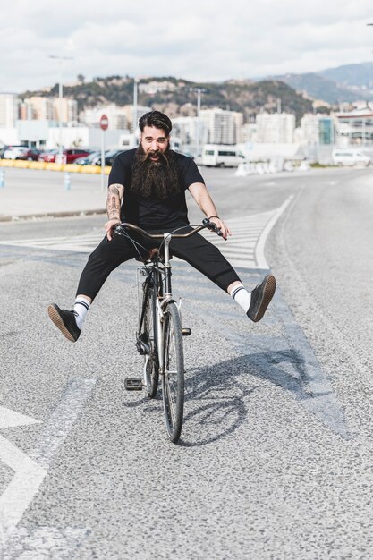 El retrato de la bicicleta del montar a caballo del hombre joven en el camino con las piernas expulsó