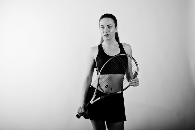 Foto gratuita retrato en blanco y negro de una hermosa joven jugadora con ropa deportiva sosteniendo una raqueta de tenis mientras se enfrenta a un fondo blanco