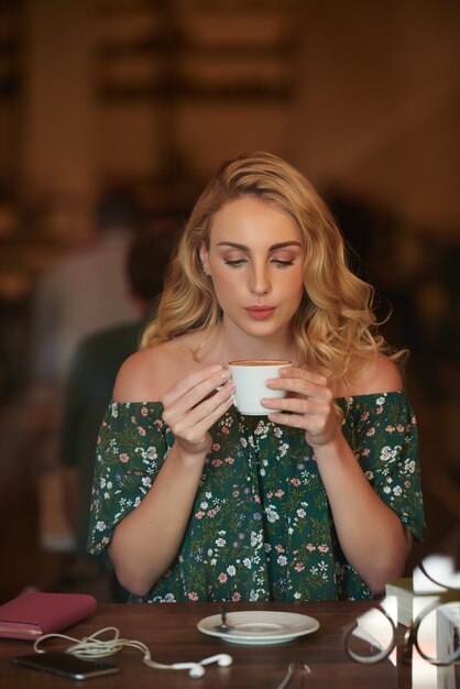 Retrato de bonita rubia sentada en la mesa de café y tomando café