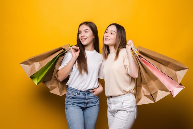 Retrato de bonitas chicas guapas atractivas con bolsas de colores divirtiéndose aislado en la pared de color amarillo