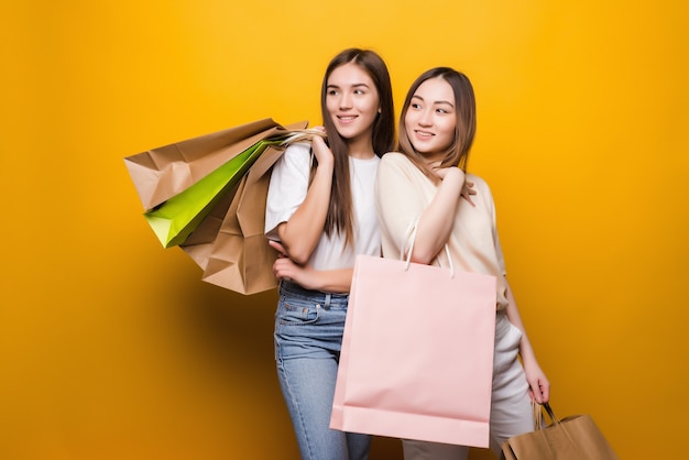 Retrato de bonitas chicas lindas abrazando sosteniendo en las manos llevando una nueva compra fresca aislada en la pared amarilla