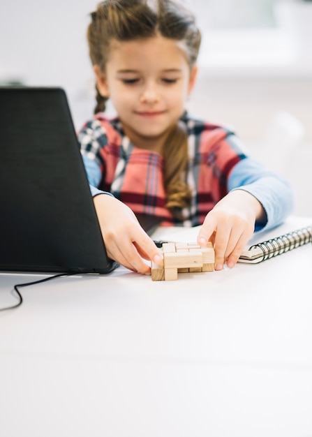 Retrato borroso de una niña jugando con rompecabezas de madera en el escritorio blanco