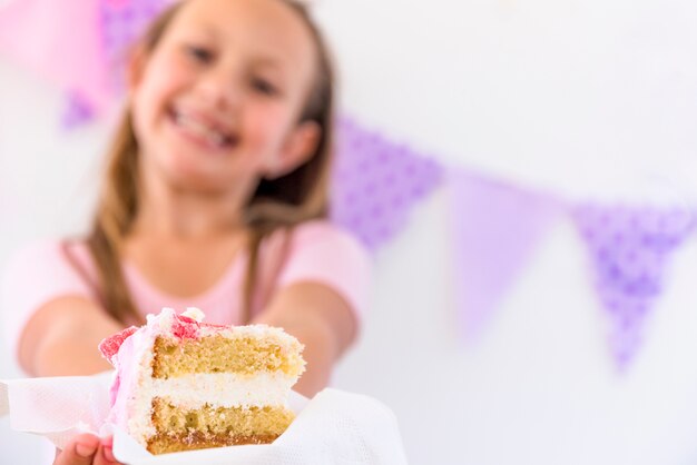 Retrato borroso de una niña sonriente que ofrece rebanada de pastel