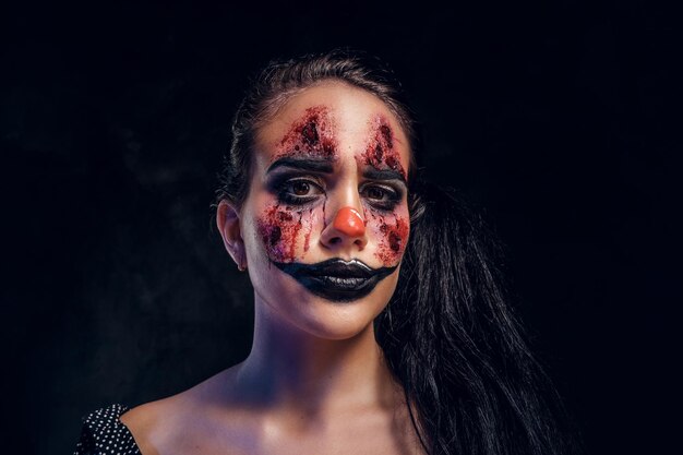 Retrato de bromista malvado espeluznante con maquillaje aterrador en un estudio fotográfico oscuro.