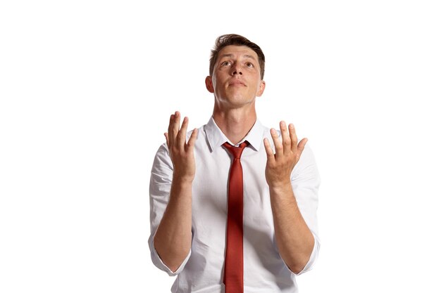 Foto gratuita retrato de un buen hombre moreno con ojos marrones, vestido con una camisa blanca y una corbata roja. está rezando mientras posa en un estudio aislado sobre un fondo blanco. concepto de gesticulación y emo sincero