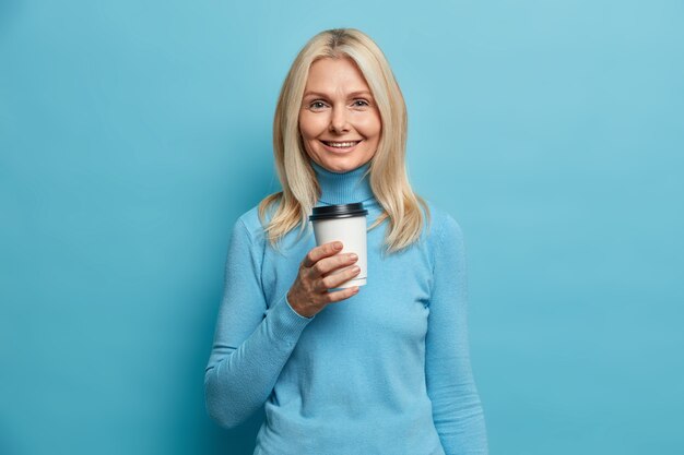 Retrato de buena mujer europea adulta sostiene una taza de café desechable