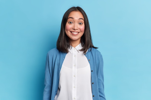 Retrato de buena mujer morena sonríe toothily escucha algo agradable viste modelos de camisa y jersey casual interior