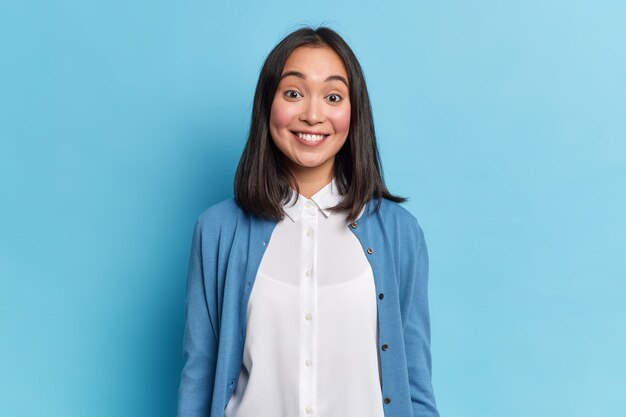 Retrato de buena mujer morena sonríe toothily escucha algo agradable viste modelos de camisa y jersey casual interior