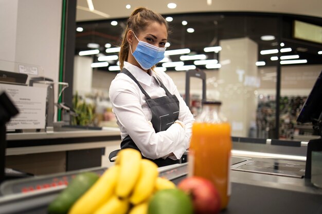 Retrato de cajero en supermercado con máscara y guantes totalmente protegidos contra el virus corona