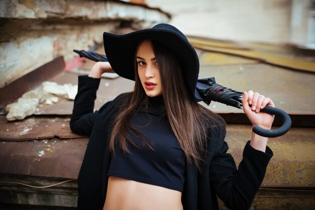 Retrato de la calle de la joven dama casual con sombrero, ropa negra, labios rojos