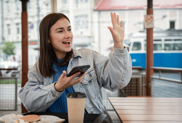 Retrato de la calle de una mujer joven alegre en la terraza de un café, que está esperando a alguien