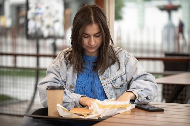 Retrato de la calle de una mujer joven con comida rápida en la terraza de verano de un café