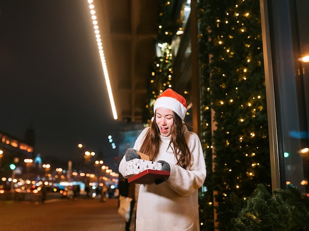 Retrato de calle de noche de joven bella mujer actuando emocionado. Guirnalda de luces festivas.