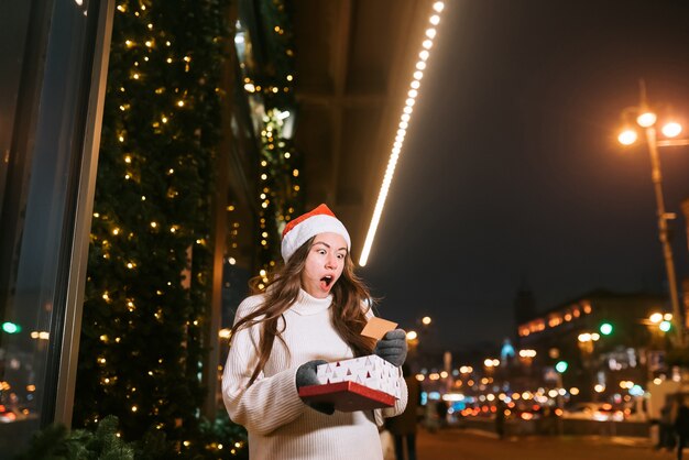 Retrato de calle de noche de joven bella mujer actuando emocionado. Guirnalda de luces festivas.