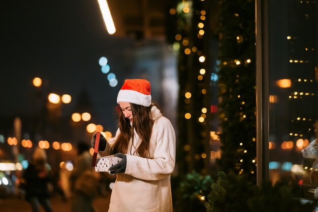 Retrato de calle de noche de joven bella mujer actuando emocionado. Guirnalda de luces festivas.