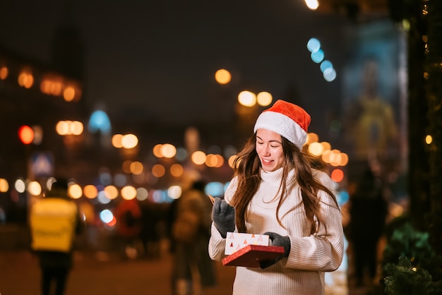 Retrato de calle de noche de joven bella mujer actuando emocionado. Guirnalda de luces festivas.