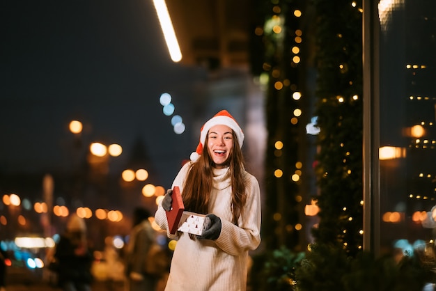 Retrato de calle de noche de mujer hermosa joven actuando emocionado. Guirnalda de luces festivas.