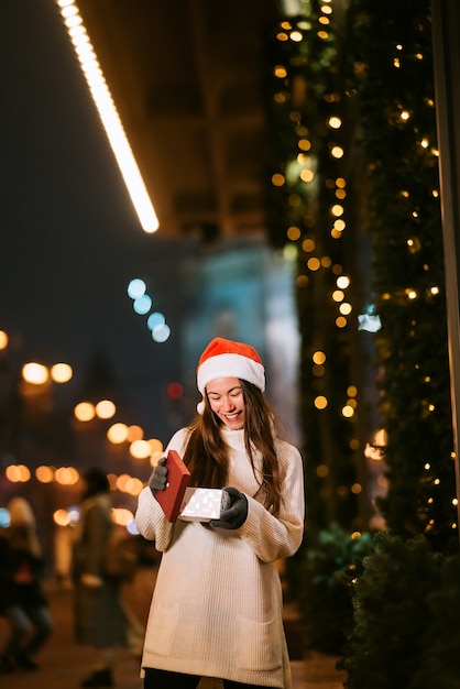 Retrato de calle de noche de mujer hermosa joven actuando emocionado. Guirnalda de luces festivas.