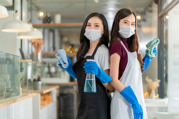 Retrato de camarera asiática con personal de delantal con protección guante de goma protección de mascarilla protección de mano toalla de limpieza y desinfectante en aerosol de alcohol para proteger las ideas de salud de infección por coronavirus