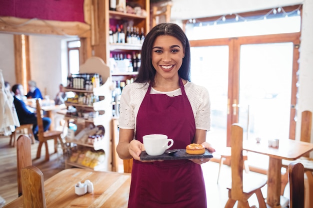 Retrato de camarera sosteniendo una taza de café y aperitivos