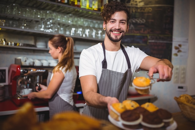 Retrato de camarero con un plato de torta de la taza en el mostrador