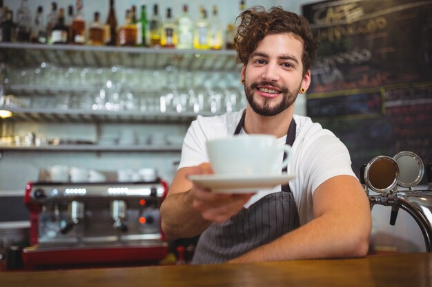 Retrato de camarero que sirve una taza de café en el mostrador