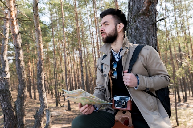 Retrato de un caminante masculino que sostiene un mapa genérico en el bosque que mira lejos