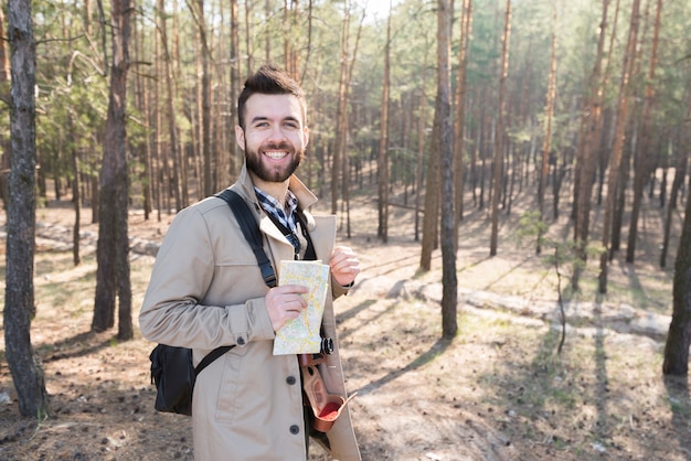 Retrato de un caminante masculino sonriente que sostiene un mapa genérico en el bosque