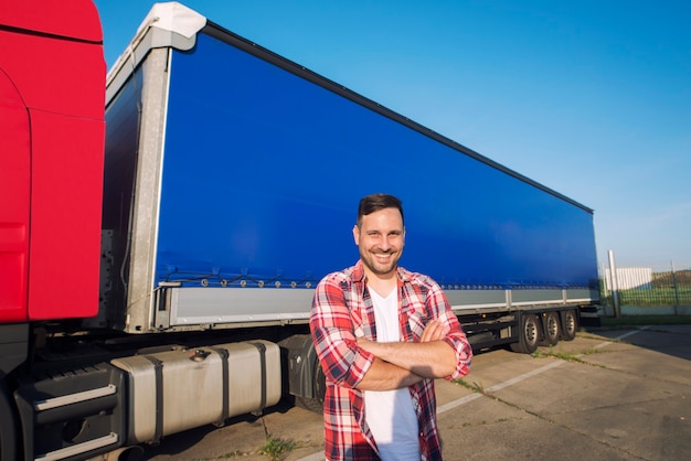 Retrato de camionero de mediana edad con los brazos cruzados de pie junto al remolque de camión listo para conducir