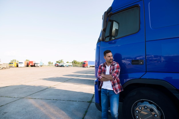 Retrato de camionero en ropa casual de pie junto a su vehículo camión y mirando hacia los lados