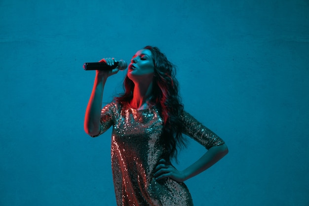 Foto gratuita retrato de cantante femenina aislado en la pared azul del estudio en luz de neón